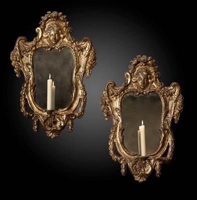 A pair of gilded mirrors, decoration with garlands and a feminine face at the top, each one with an iron arm of light, Italy, 18th century (90 cm high, 60 cm wide) ( 3 ft high, 2 ft wide)